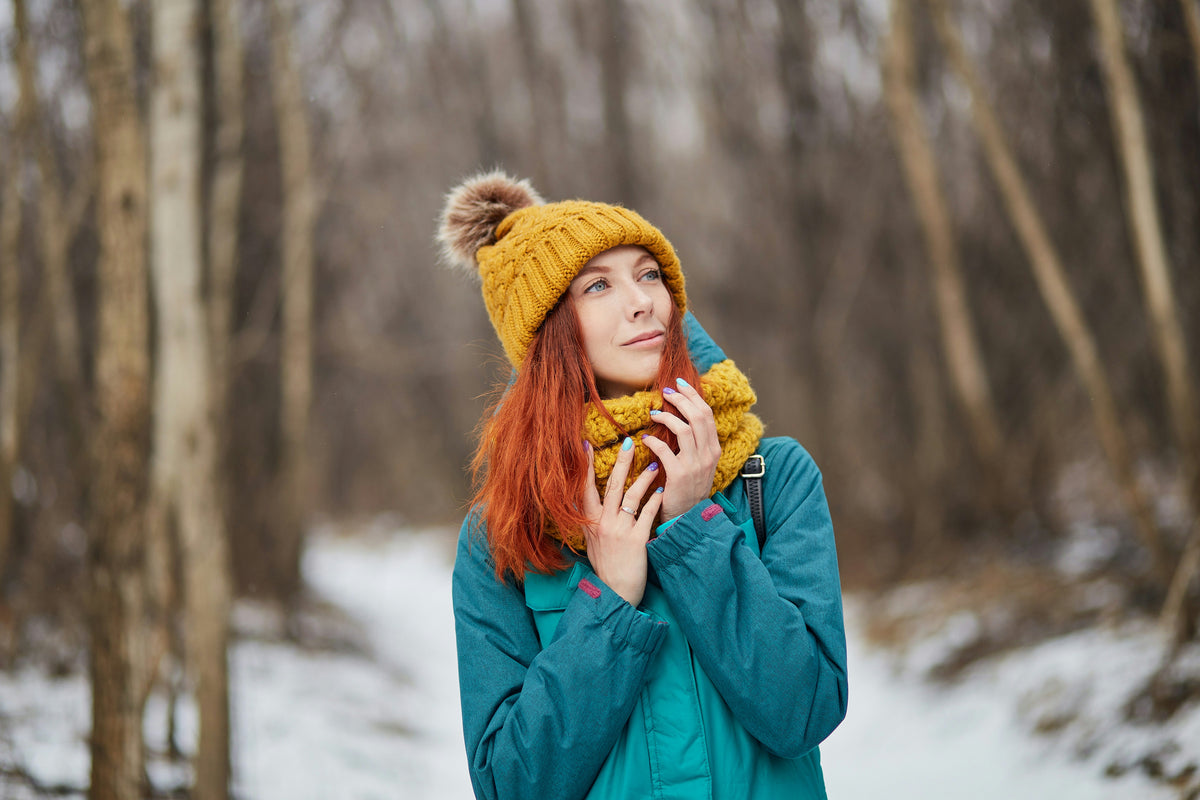 Woman wearing a yellow knit hat and scarf in a snowy forest